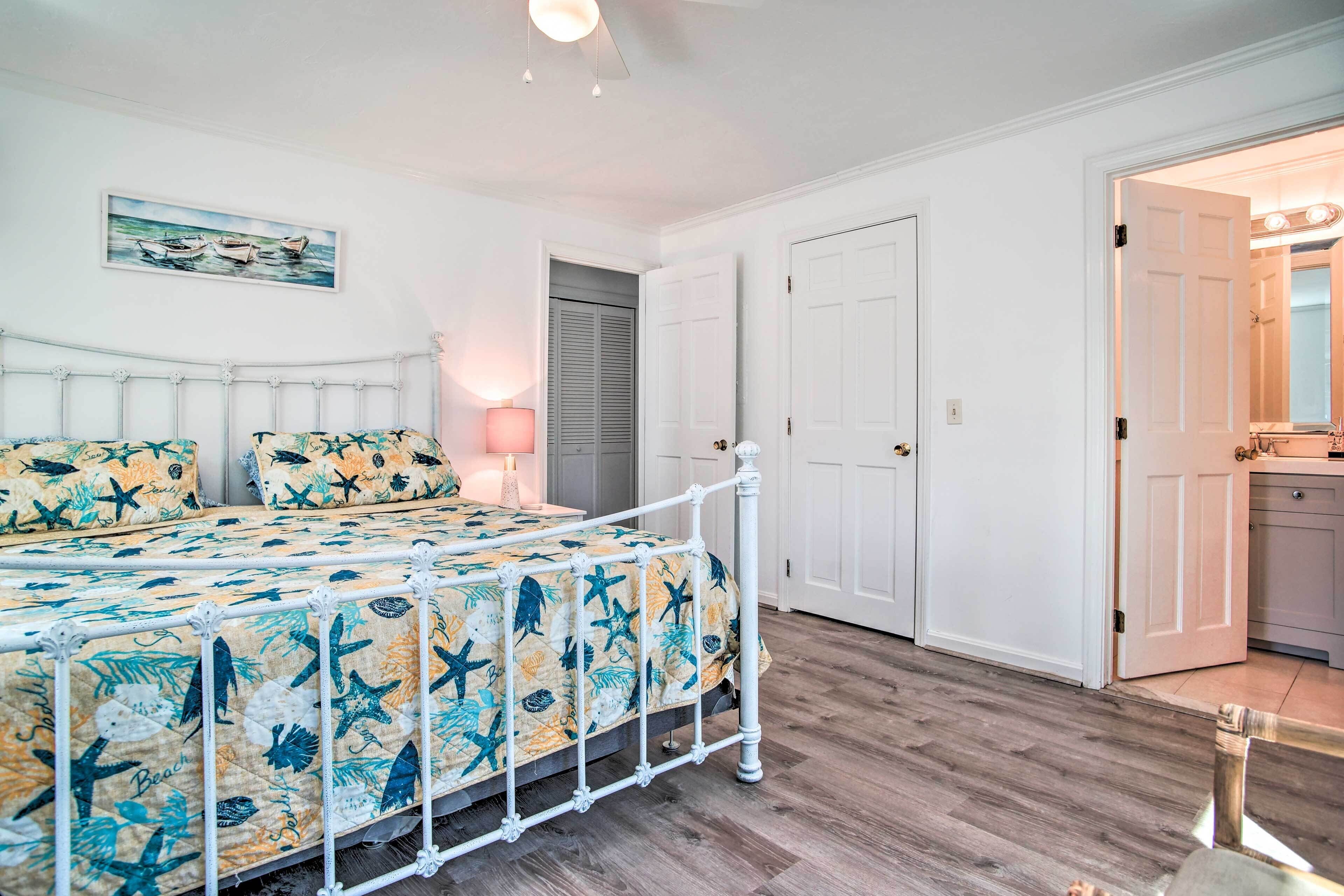 A bedroom with a bed, a nightstand, a lamp, and a door leading to a bathroom.