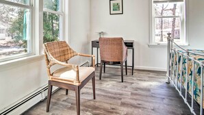 A room with two wicker chairs, a small table, and a radiator. There are large windows providing a view of trees and a building outside. - Cape Cod Escape ~ 2 Mi To Beaches & Dining! (South Yarmouth)