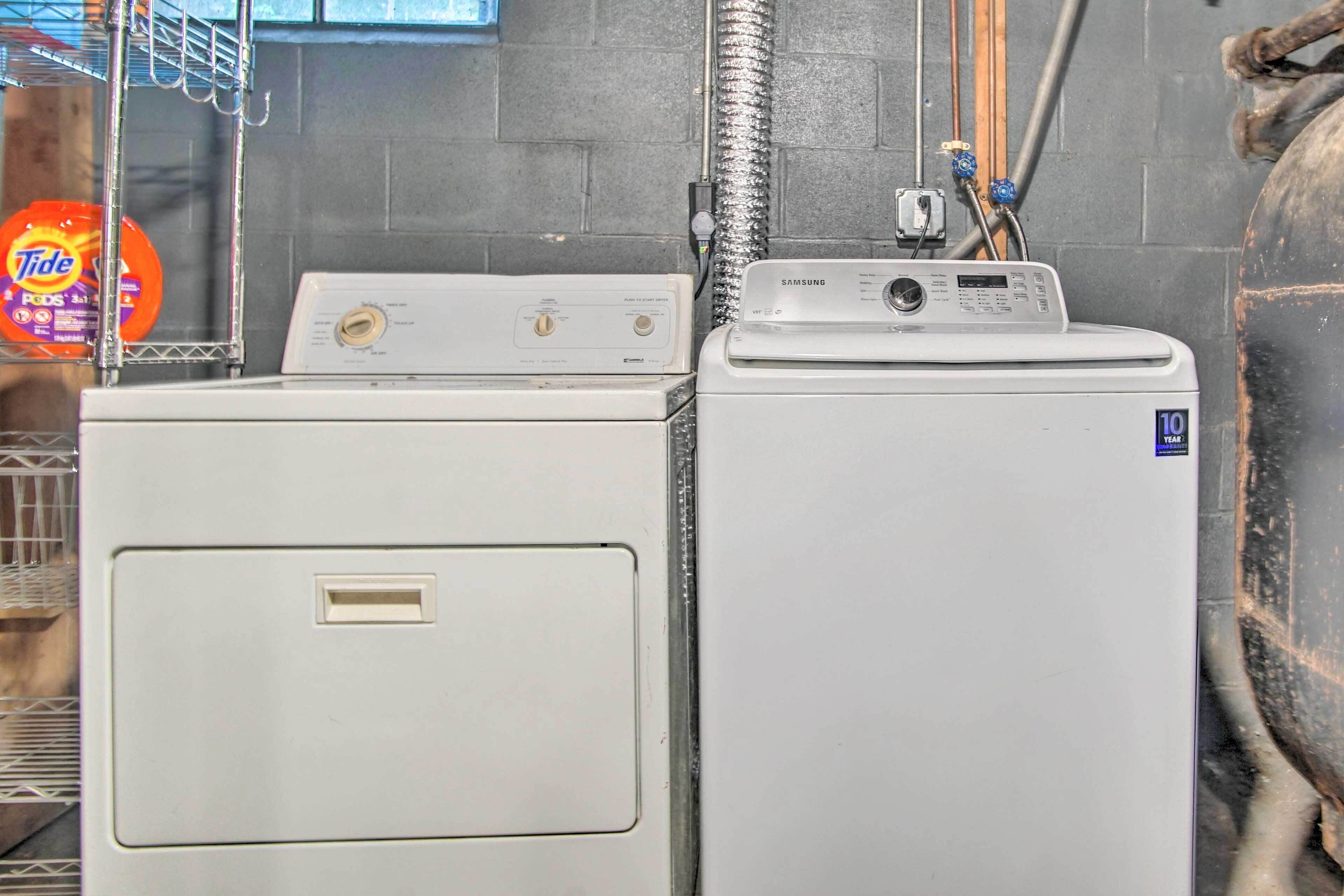 Two stacked washers in a utility room with a visible water pipe and a detergent bottle.