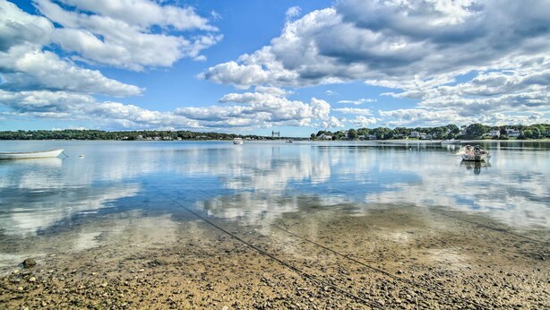 A calm lake with boats, clear skies, and a distant shoreline with buildings. - Coastal Comfort Near the Bay! 'buttermilk Cottage' (Buzzards Bay)