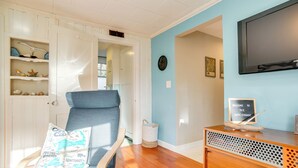 A room with a wooden floor, a blue chair with a map-themed pillow, a wooden console table with a welcome sign, and a wall-mounted TV.