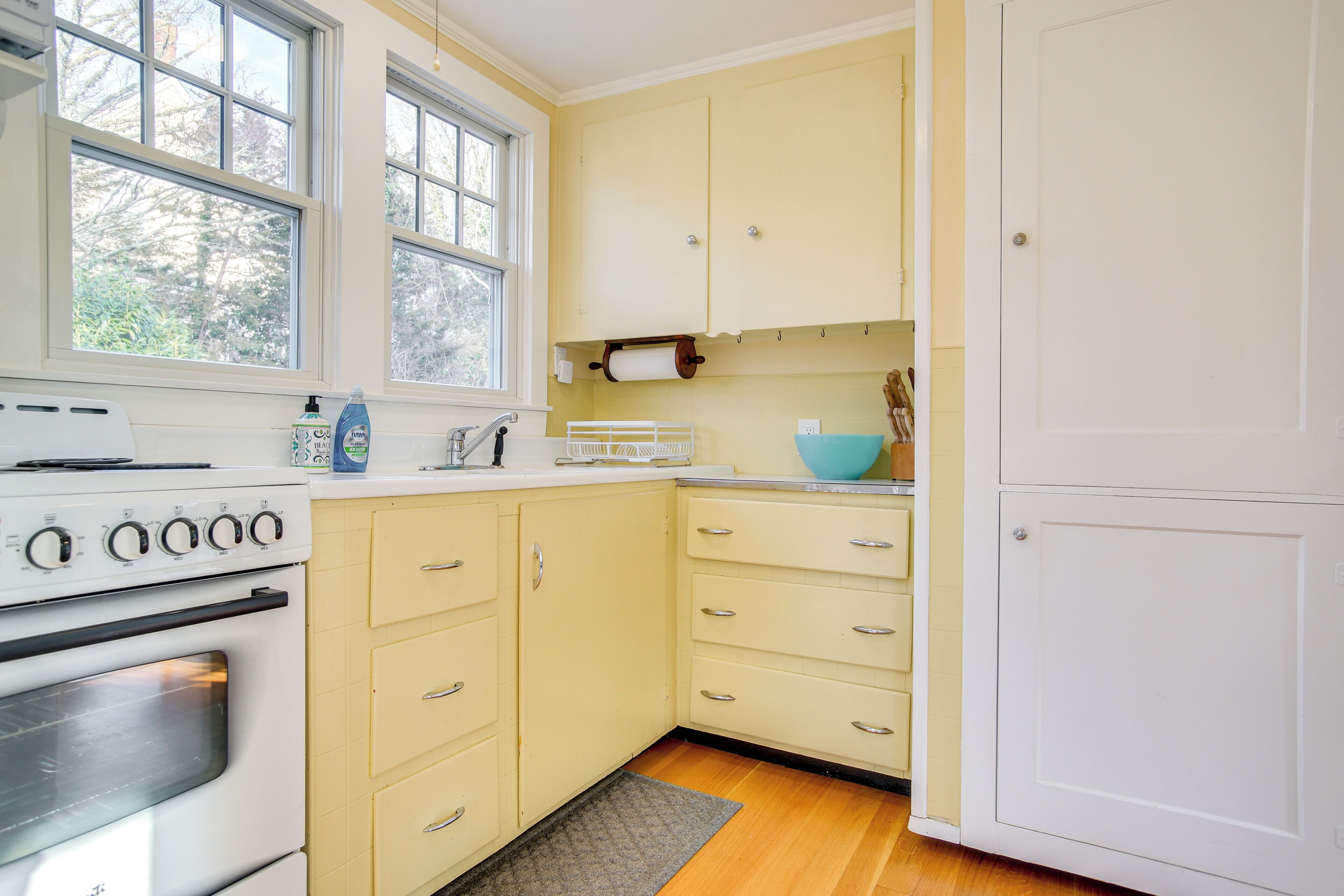 A kitchen with a white stove, yellow cabinets, and a window.