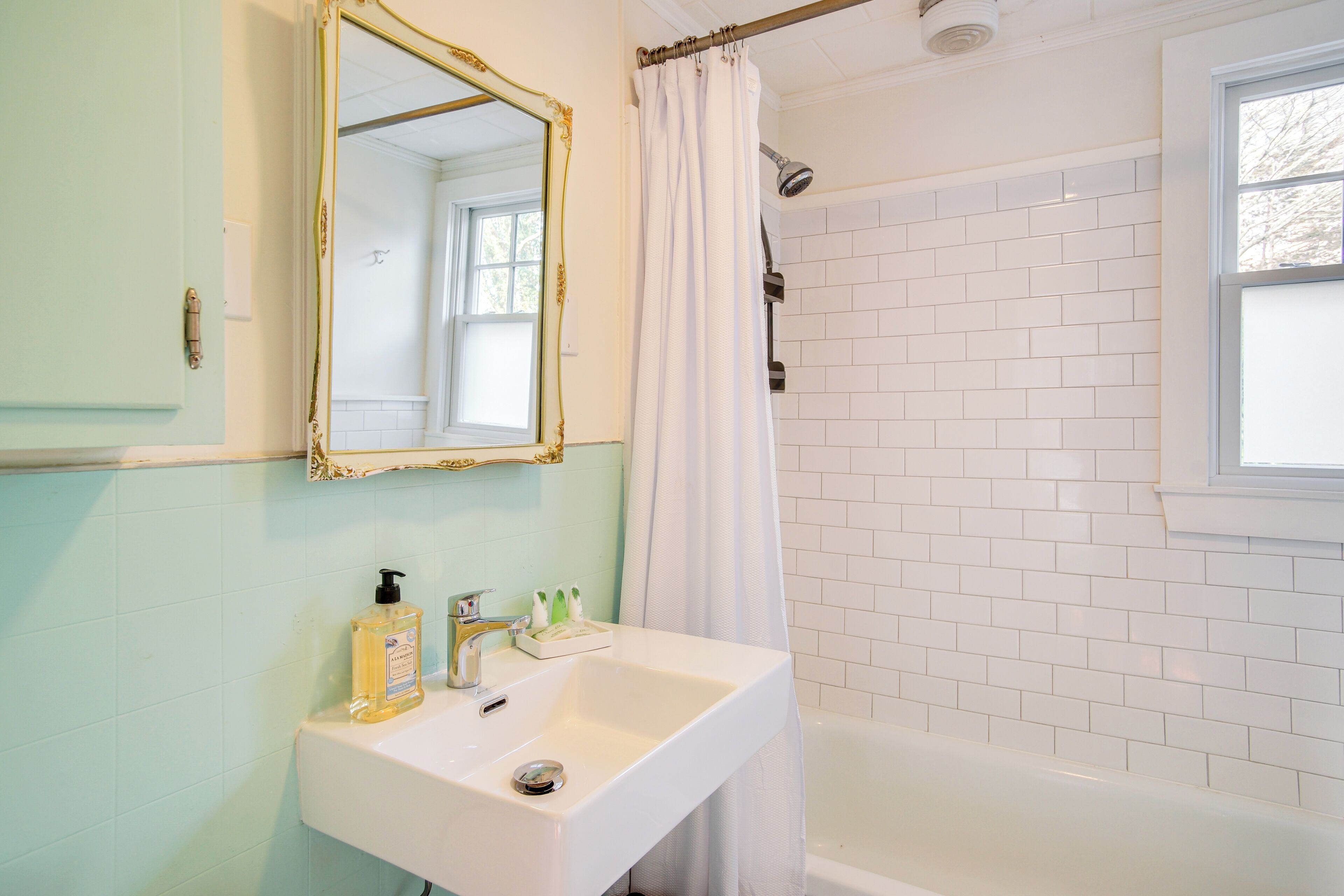 A bathroom with a white sink, a mirror with a gold frame, a shower curtain, and white tiled walls.