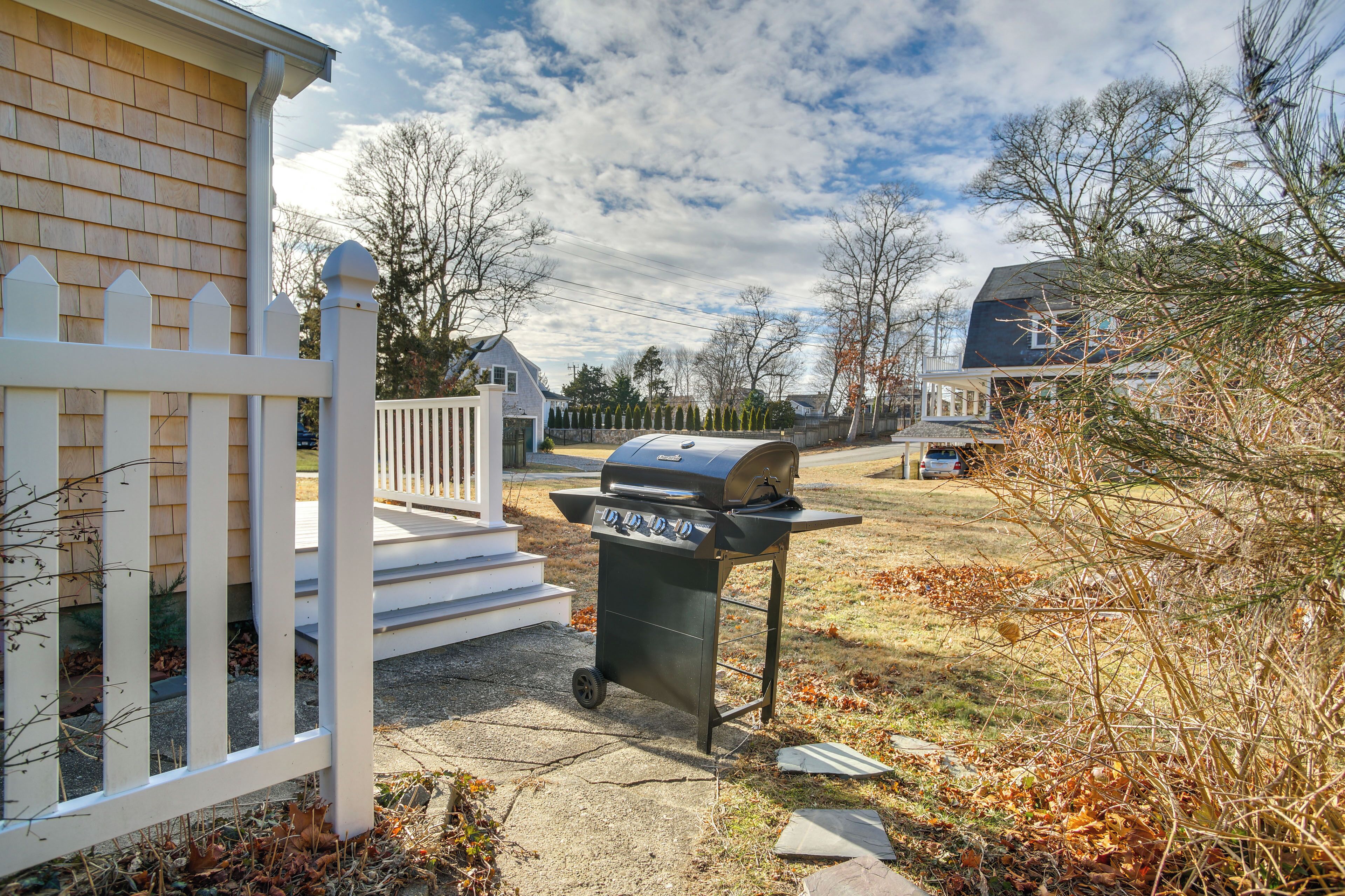 A backyard with a barbecue grill, a white picket fence, and a house with a porch.