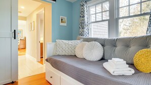A bedroom with a bed, a bedside table, a window with curtains, and a door leading to another room.