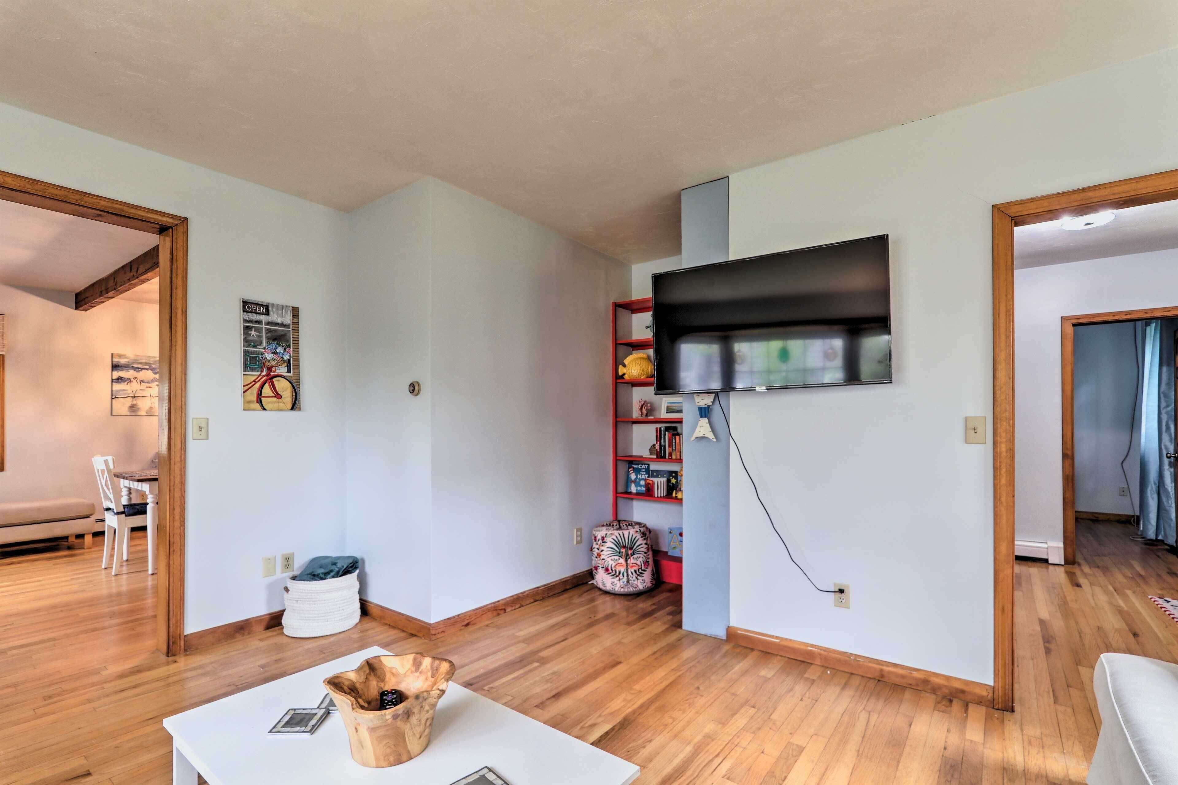 A modern living room with a wooden floor, a white table, and a television mounted on the wall.