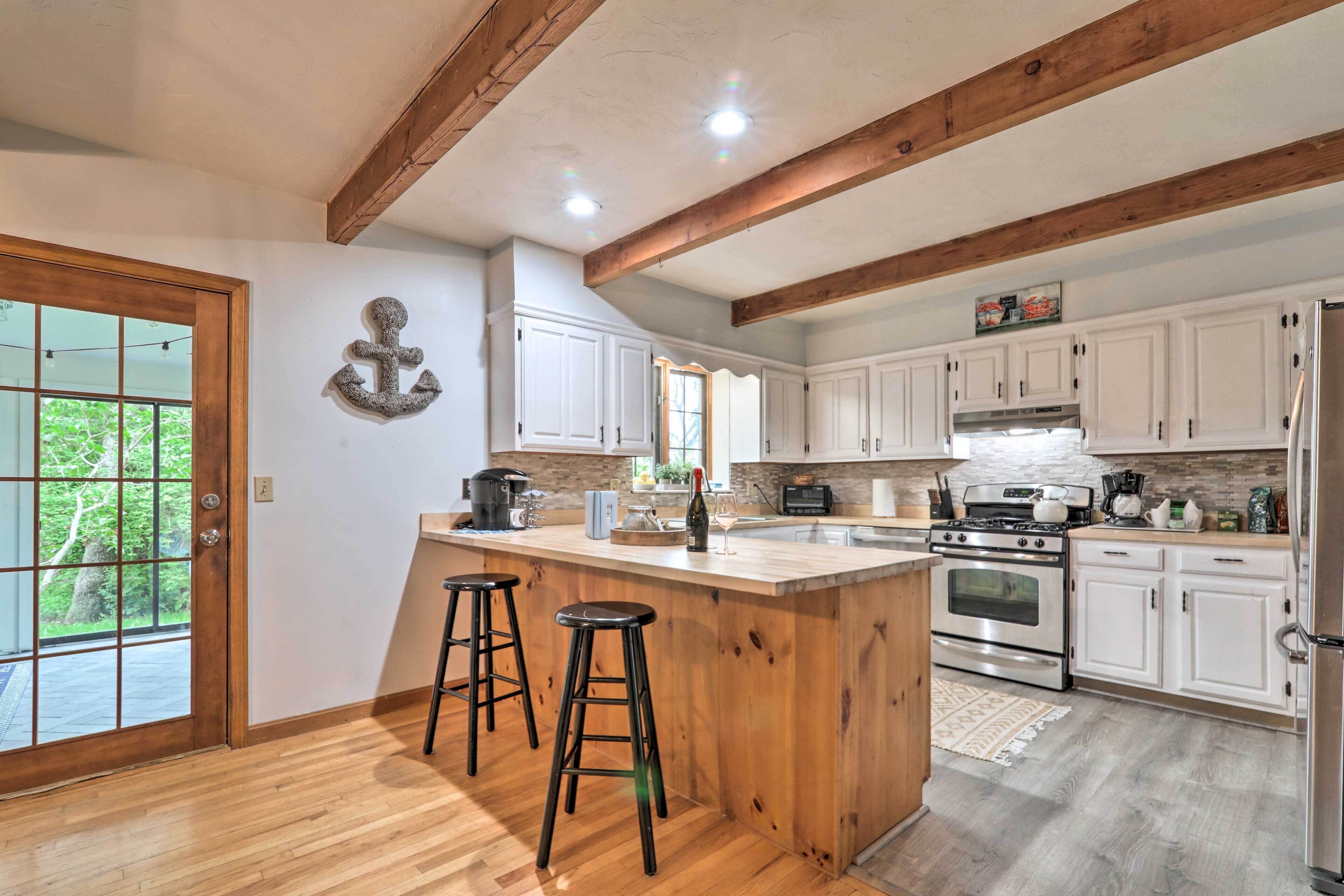 A kitchen with wooden beams, white cabinets, a large island with stools, and a view through a glass door.