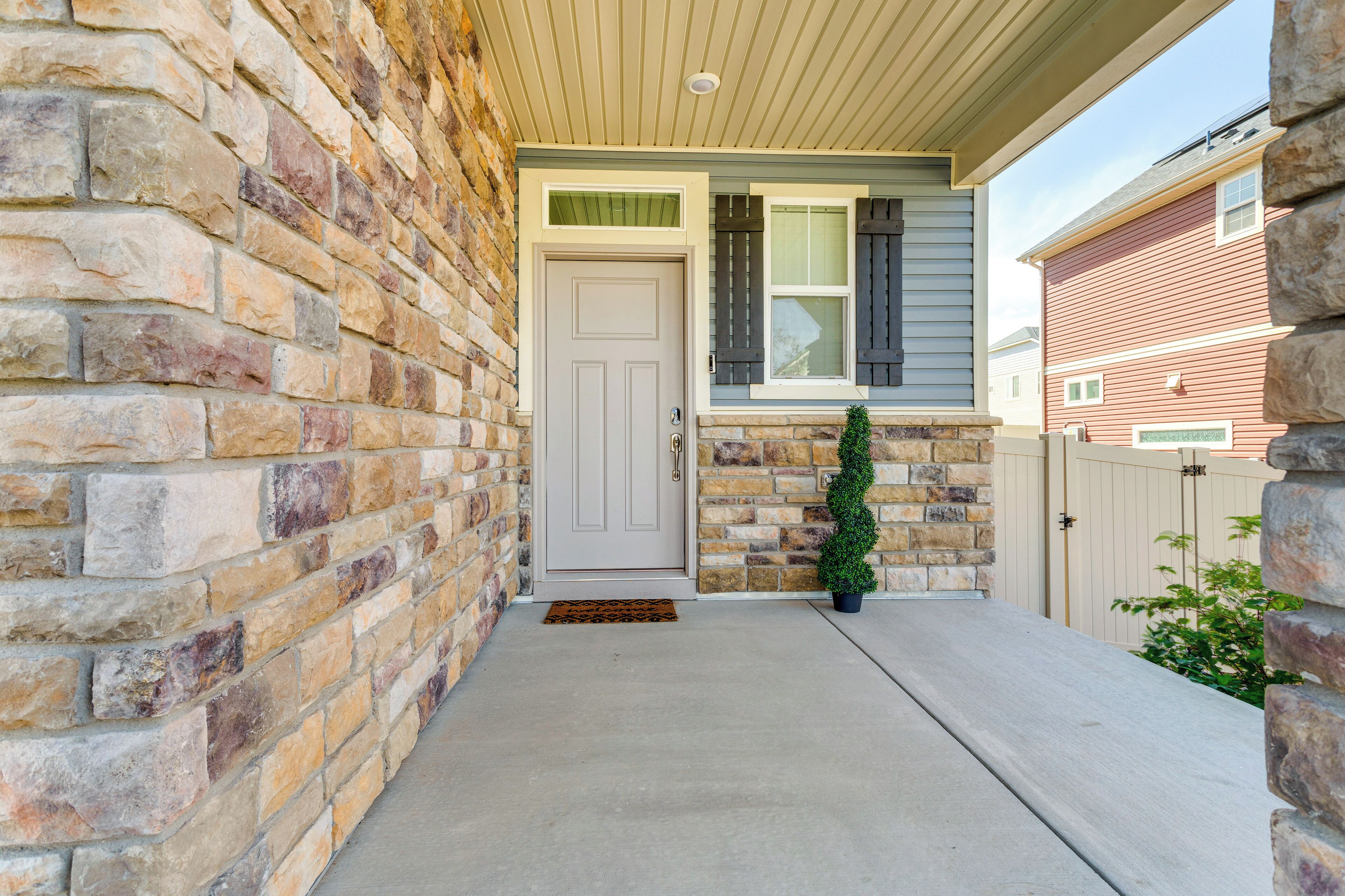 A house with a stone facade, a front door, a small porch, and a potted plant.