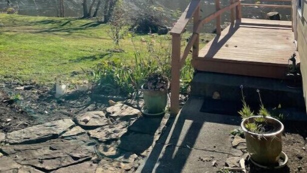 Een houten terras met een leuning, met uitzicht op een grasveld en een beboste heuvel.