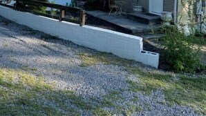 Een klein, laag huis met een groen dak, een veranda met een tafel en stoelen, en een grindpad.