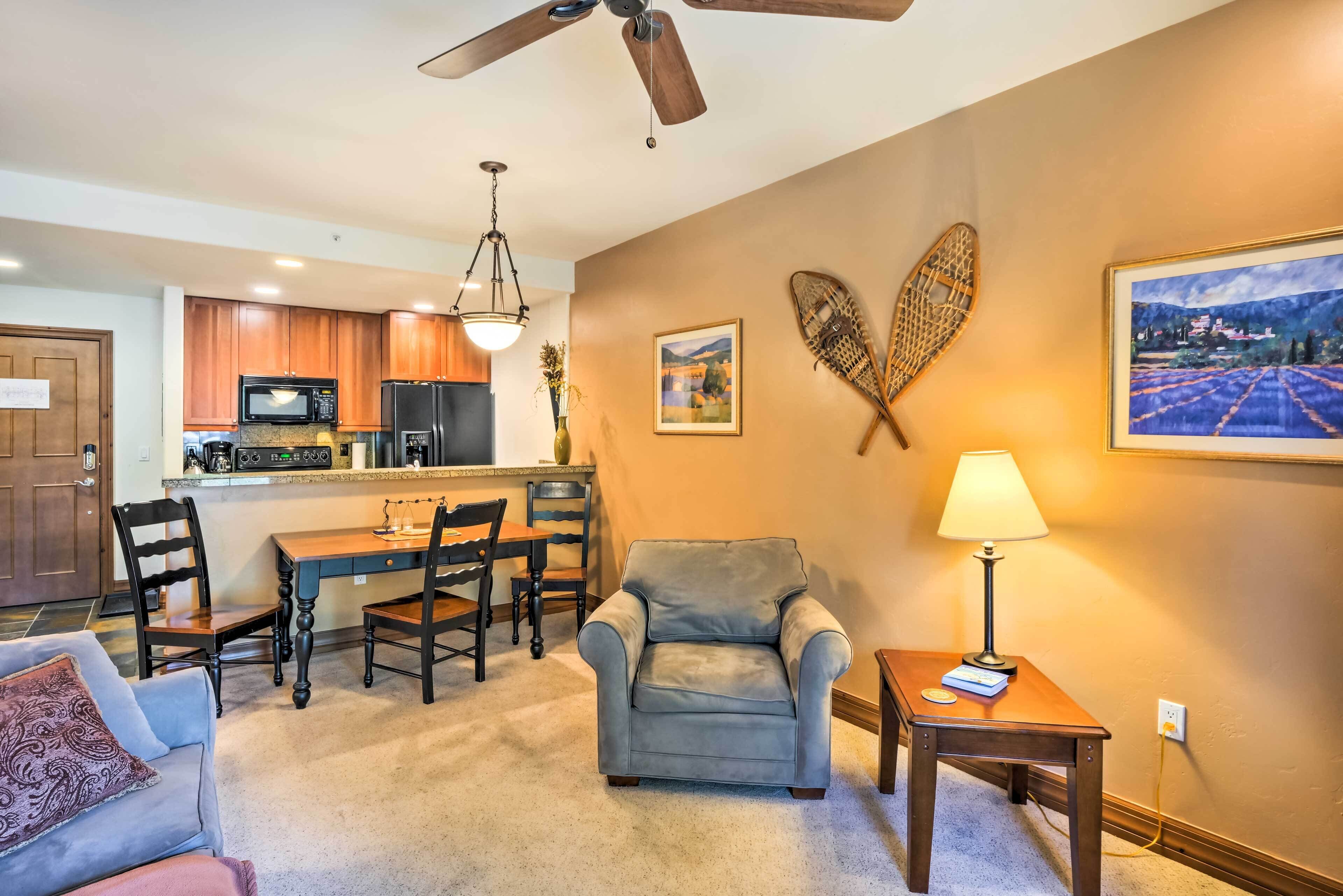 A living room with a gray armchair, a wooden coffee table, and a dining area with a wooden table and chairs.