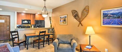 A living room with a gray armchair, a wooden coffee table, and a dining area with a wooden table and chairs.