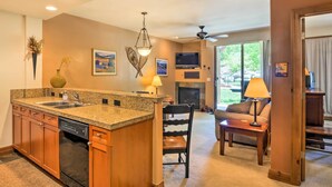 A modern kitchen with granite countertops, wooden cabinets, and a built-in dishwasher. There is a dining area with a table and chairs, a fireplace, and a ceiling fan. - 4 Mi to Breckenridge Resort: Condo w/ Sauna Access (Breckenridge)