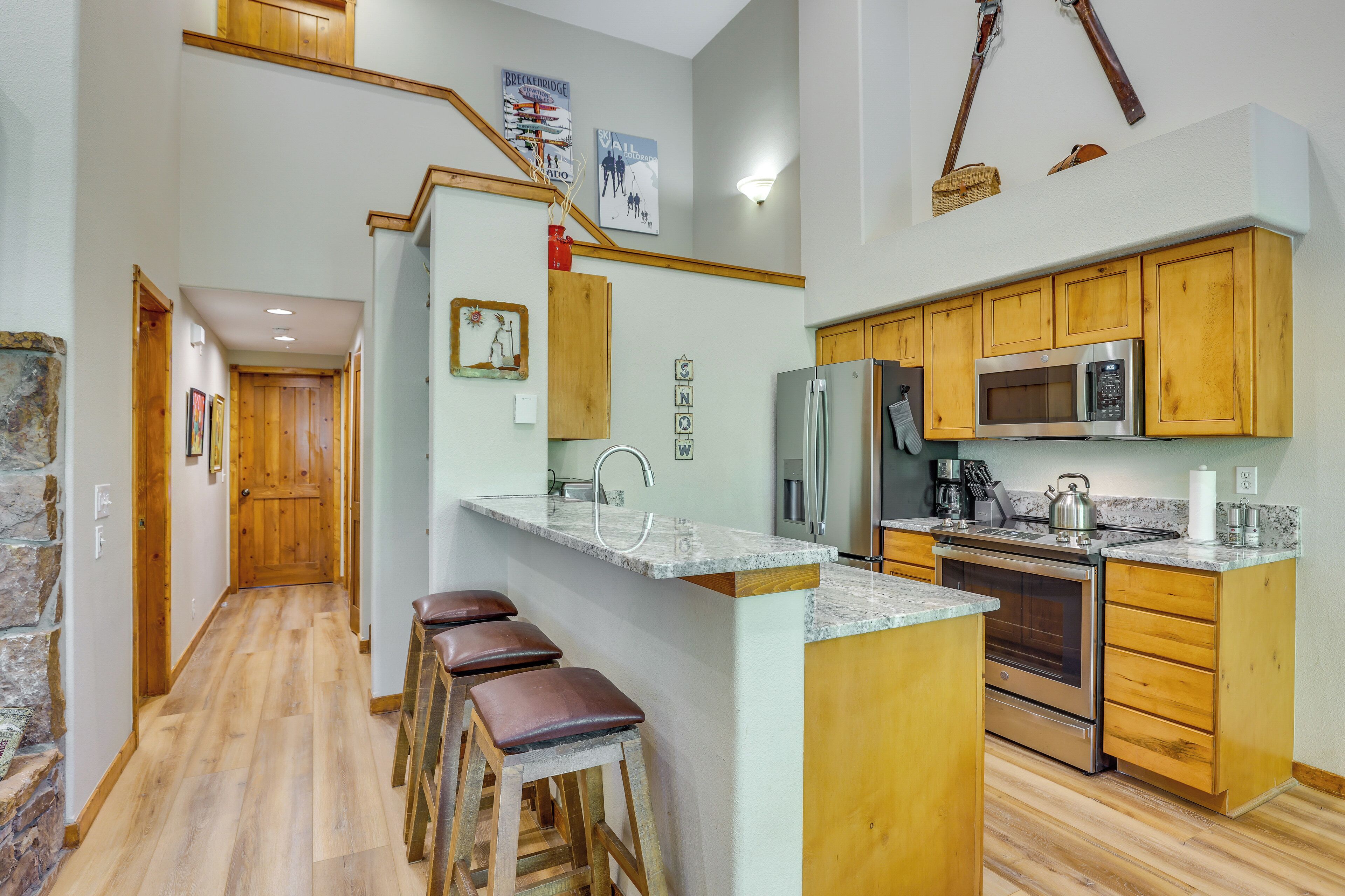 A kitchen with wooden cabinets, a stainless steel refrigerator, a microwave, and a stove. There is a wooden bar counter with stools.