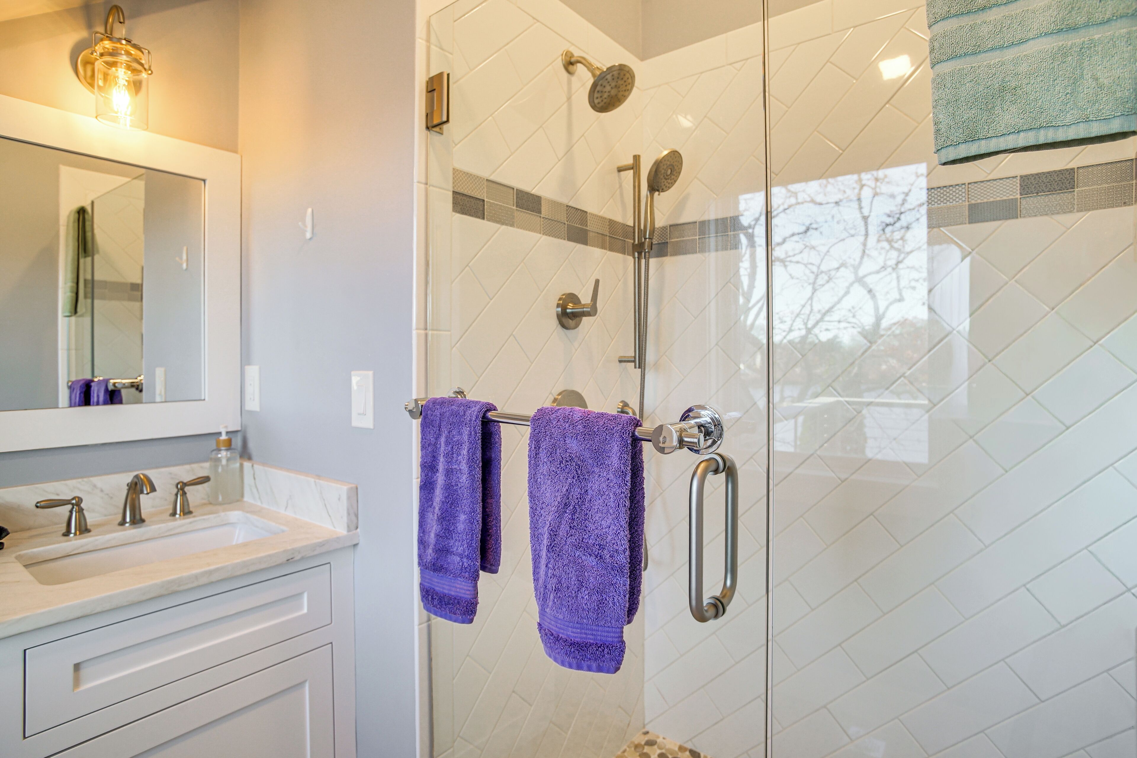 A bathroom with a glass-enclosed shower, a vanity with a sink and mirror, and two purple towels hanging on a metal towel rack.
