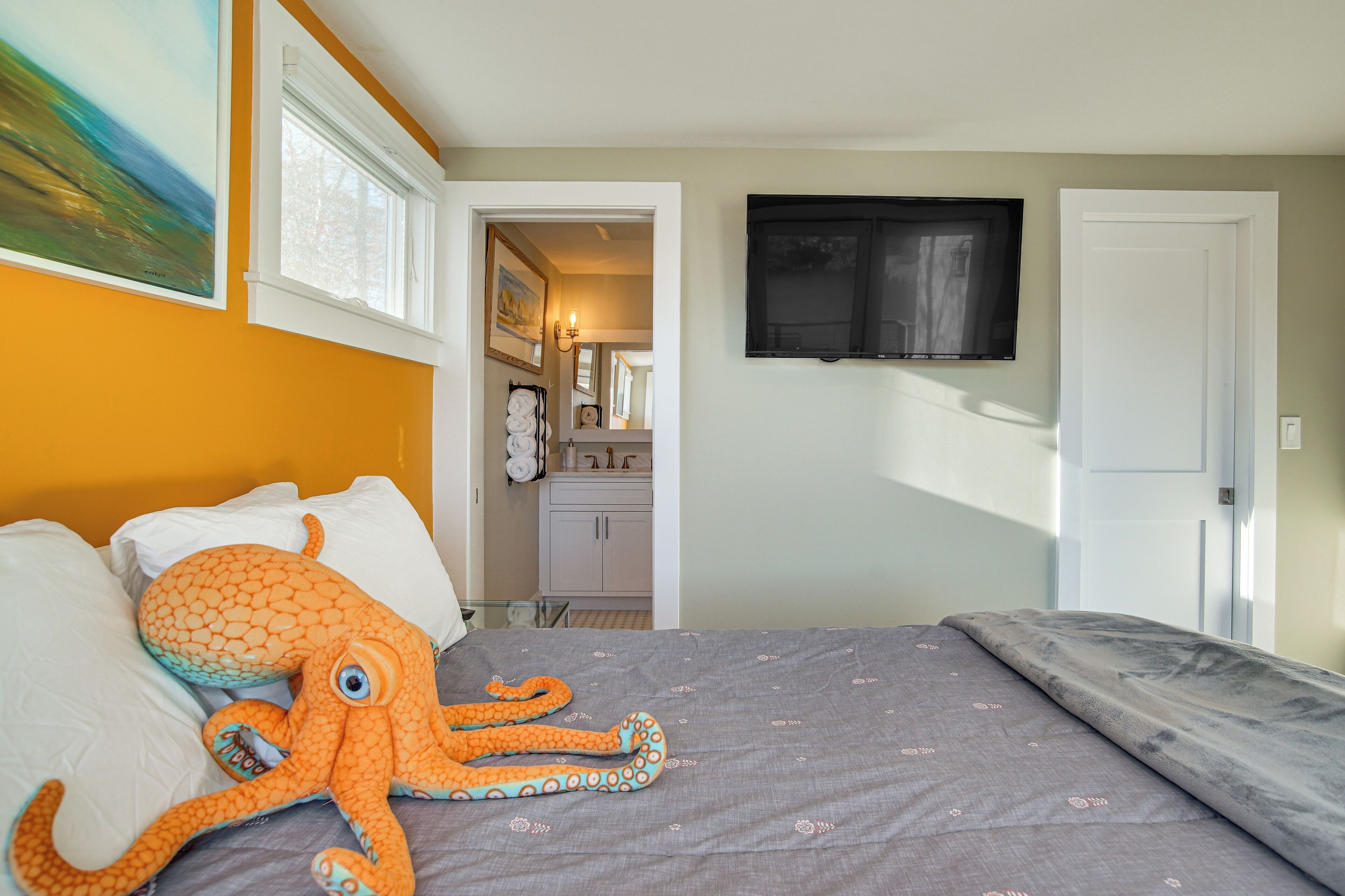A bedroom with a bed, an octopus plush toy, a television, and a bathroom visible through an open door.