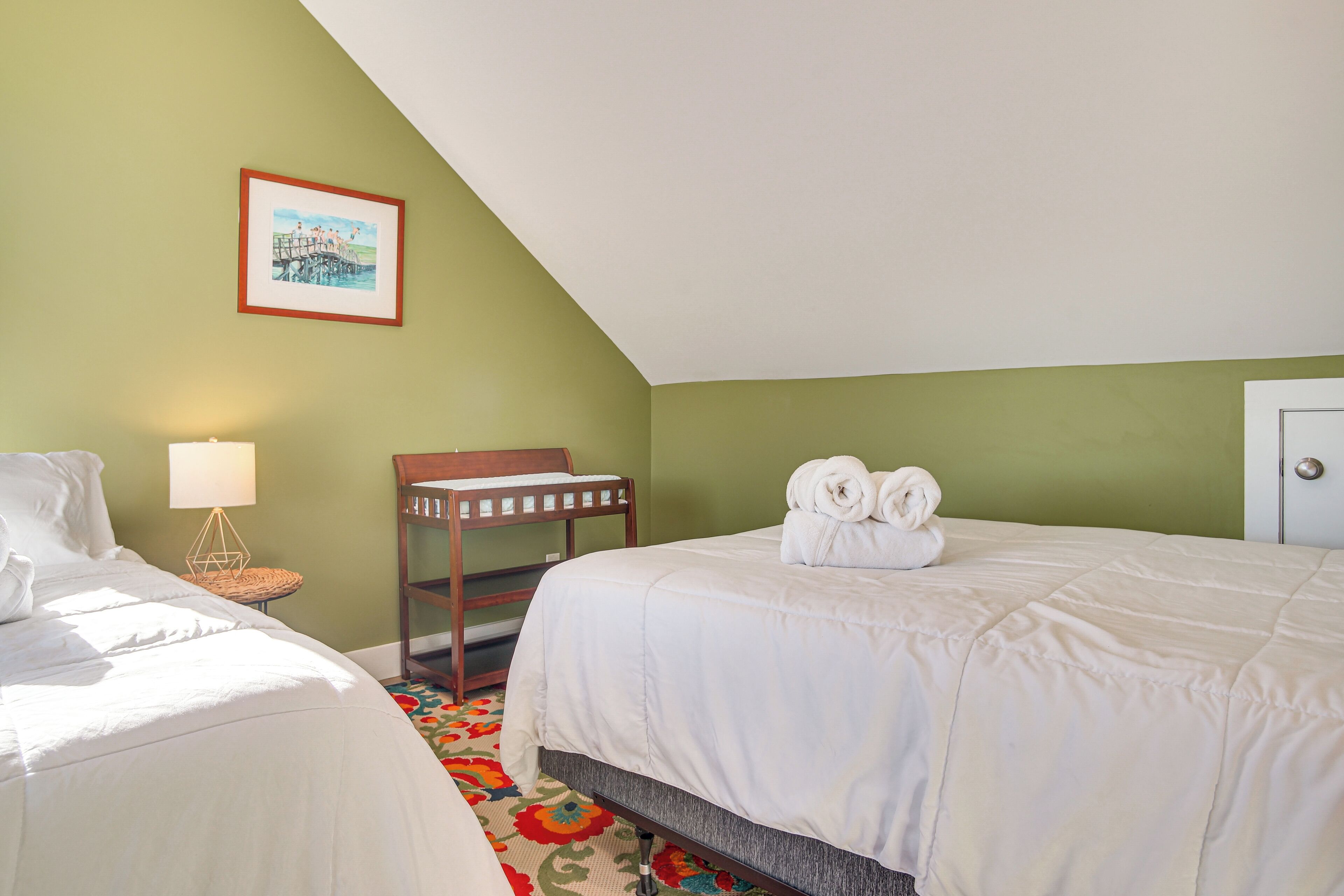 Una habitación de hotel con dos camas, un cuadro en la pared, una silla de madera y una lámpara.