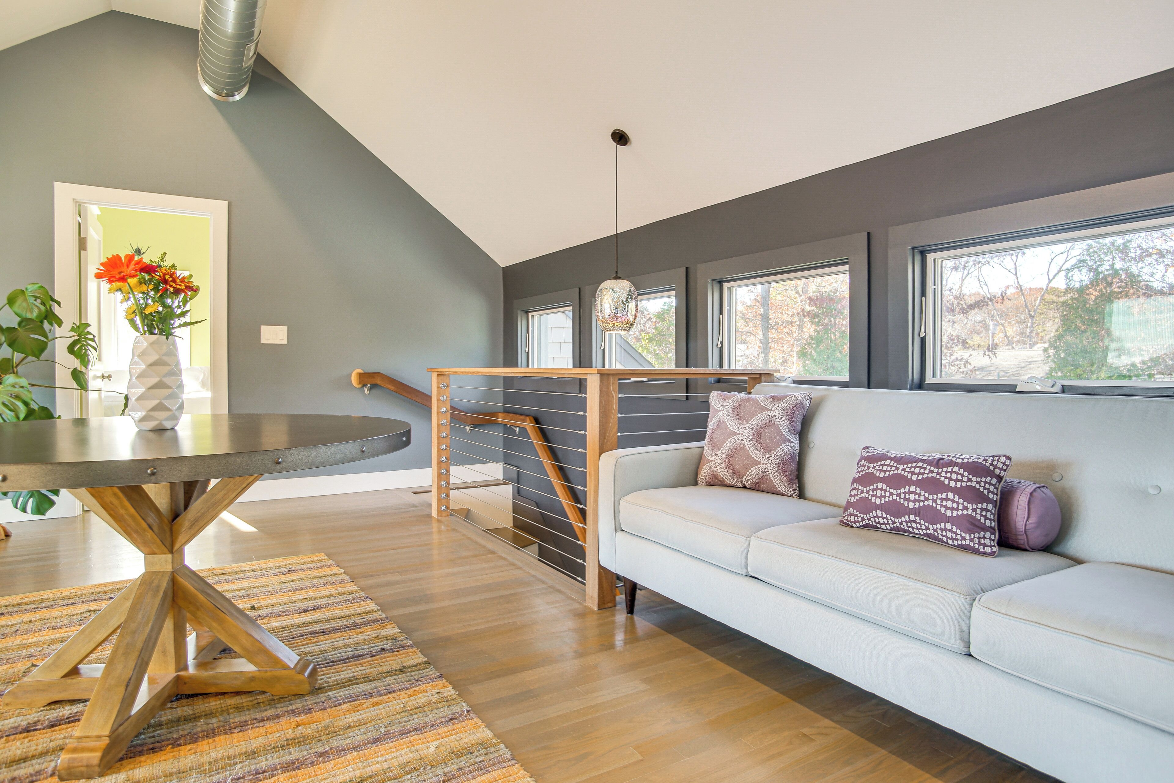 A modern living room with a white sofa, a round wooden table, and a staircase with a railing.