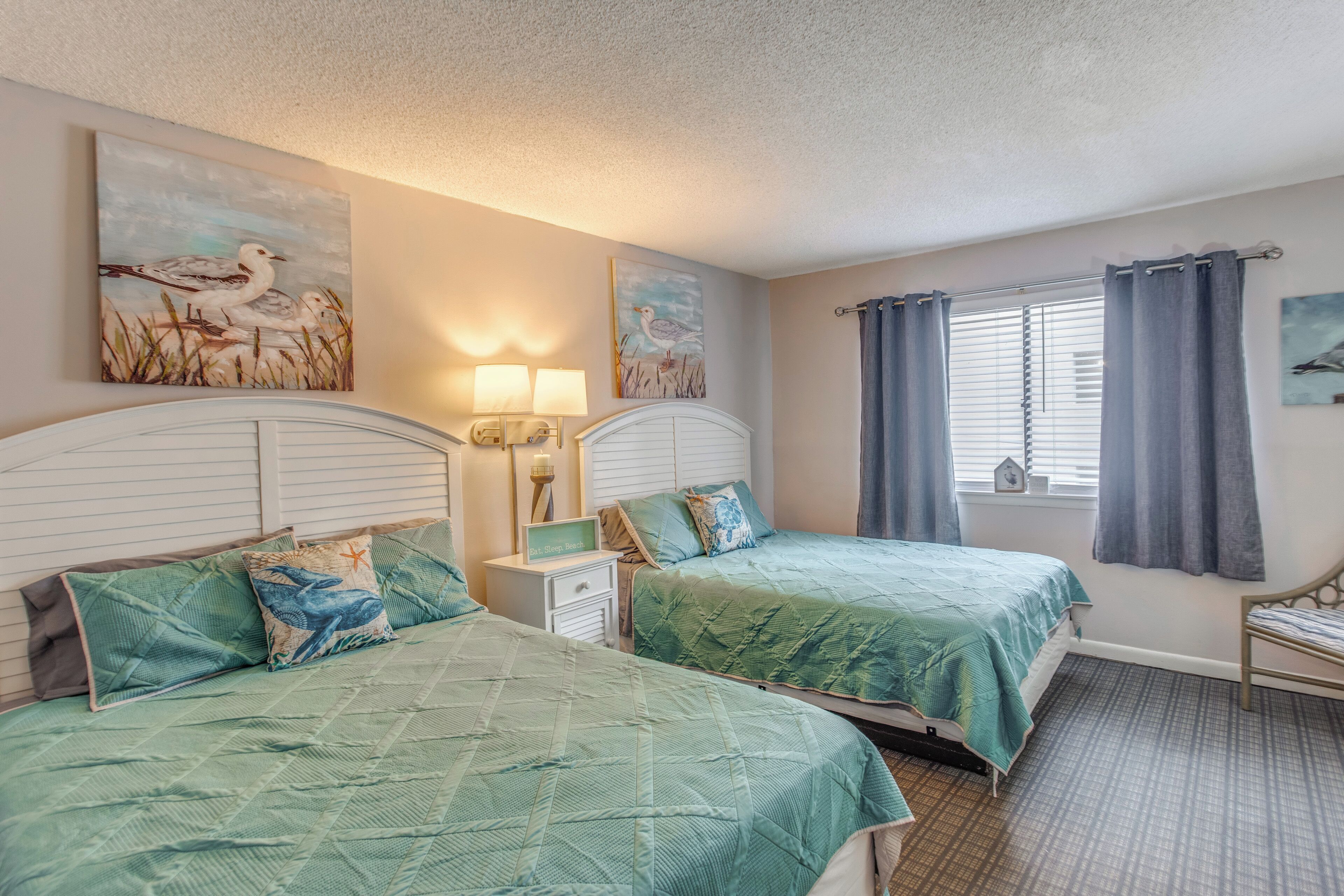 A bedroom with two beds, a nightstand, a lamp, and artwork on the walls.