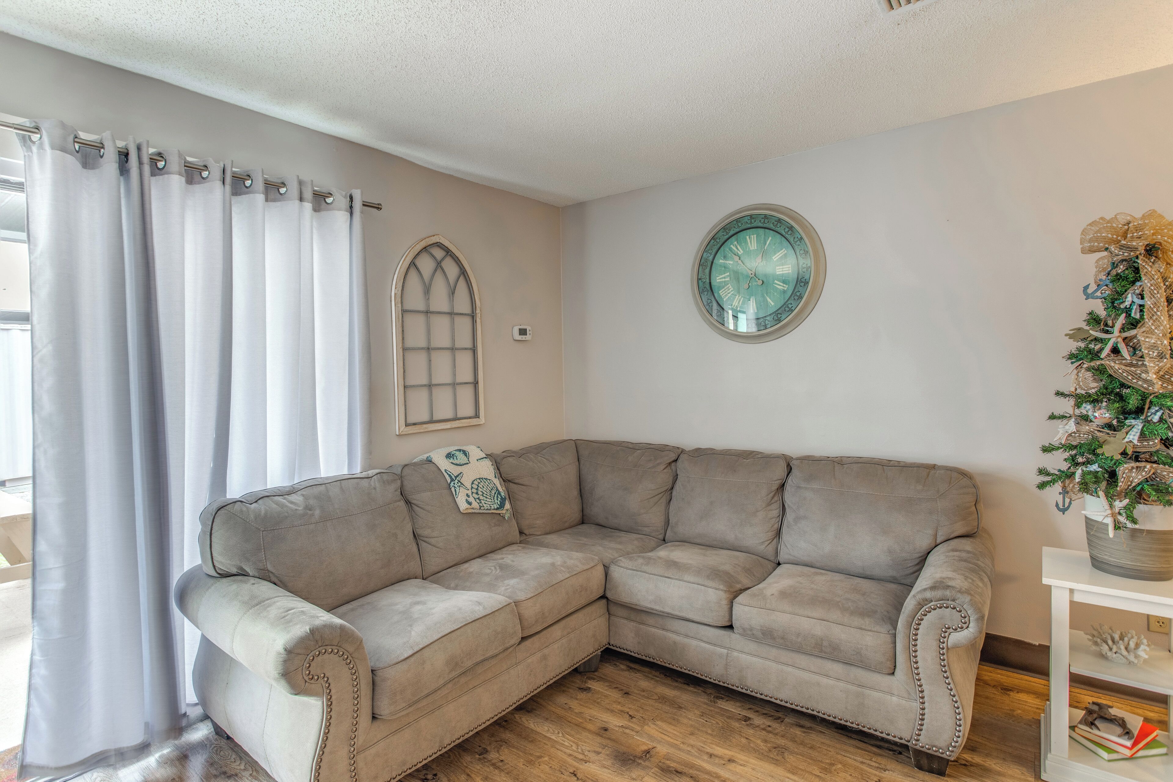 Una sala de estar en esquina con un sofá seccional beige, un reloj de pared decorativo y una pequeña planta en maceta.