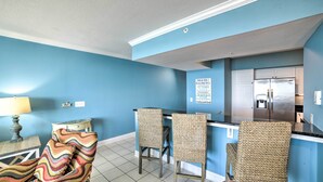 A kitchen with blue walls, a refrigerator, and two wicker chairs. - Spectacular Oceanfront Emerald Beach Resort Condo (Panama City Beach)