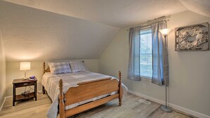 A bedroom with a wooden bed, a nightstand with a lamp, a window with curtains, and a wall decoration. - Updated Plymouth Home < 2 Miles to Waterfront! (Plymouth)