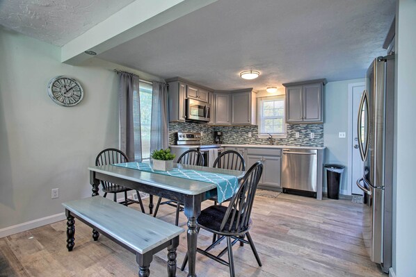 A modern kitchen with a dining area, featuring a wooden table, chairs, and a clock on the wall. - Updated Plymouth Home < 2 Miles to Waterfront! (Plymouth)