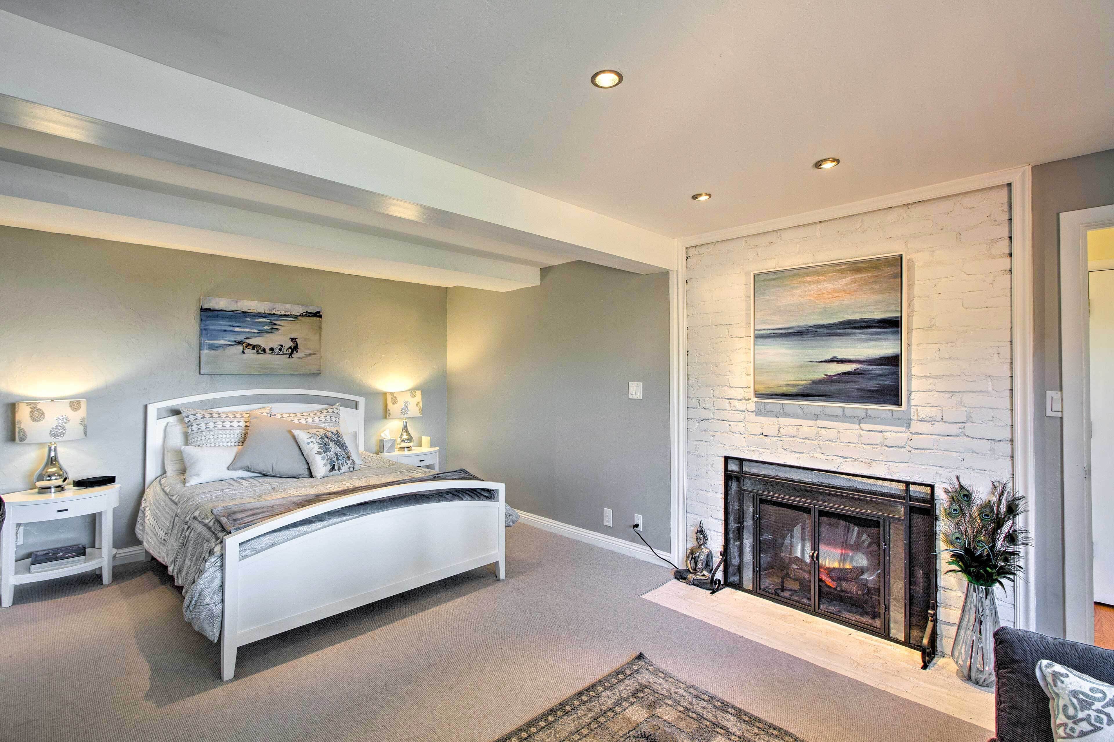 A bedroom with a bed, bedside tables, a fireplace, and artwork on the walls.