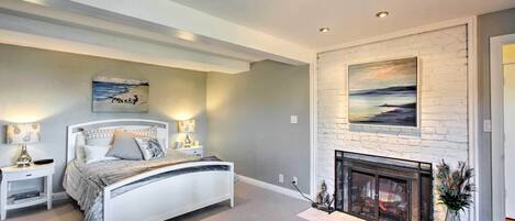 A bedroom with a bed, bedside tables, a fireplace, and artwork on the walls.