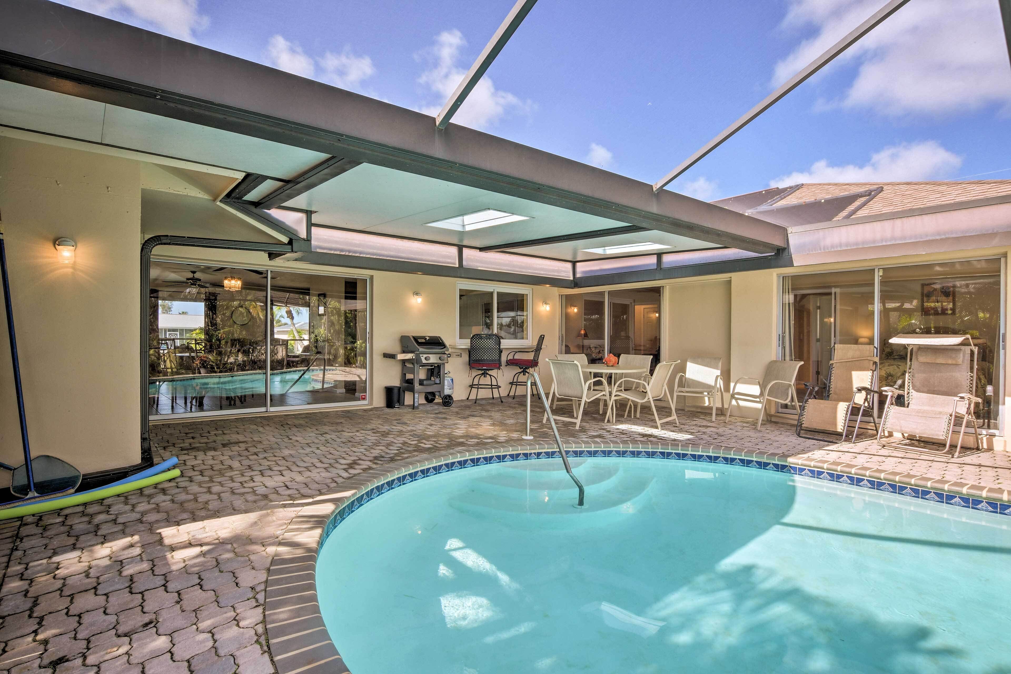 A swimming pool with a tiled border, a covered patio area with outdoor furniture, and a view of the backyard.