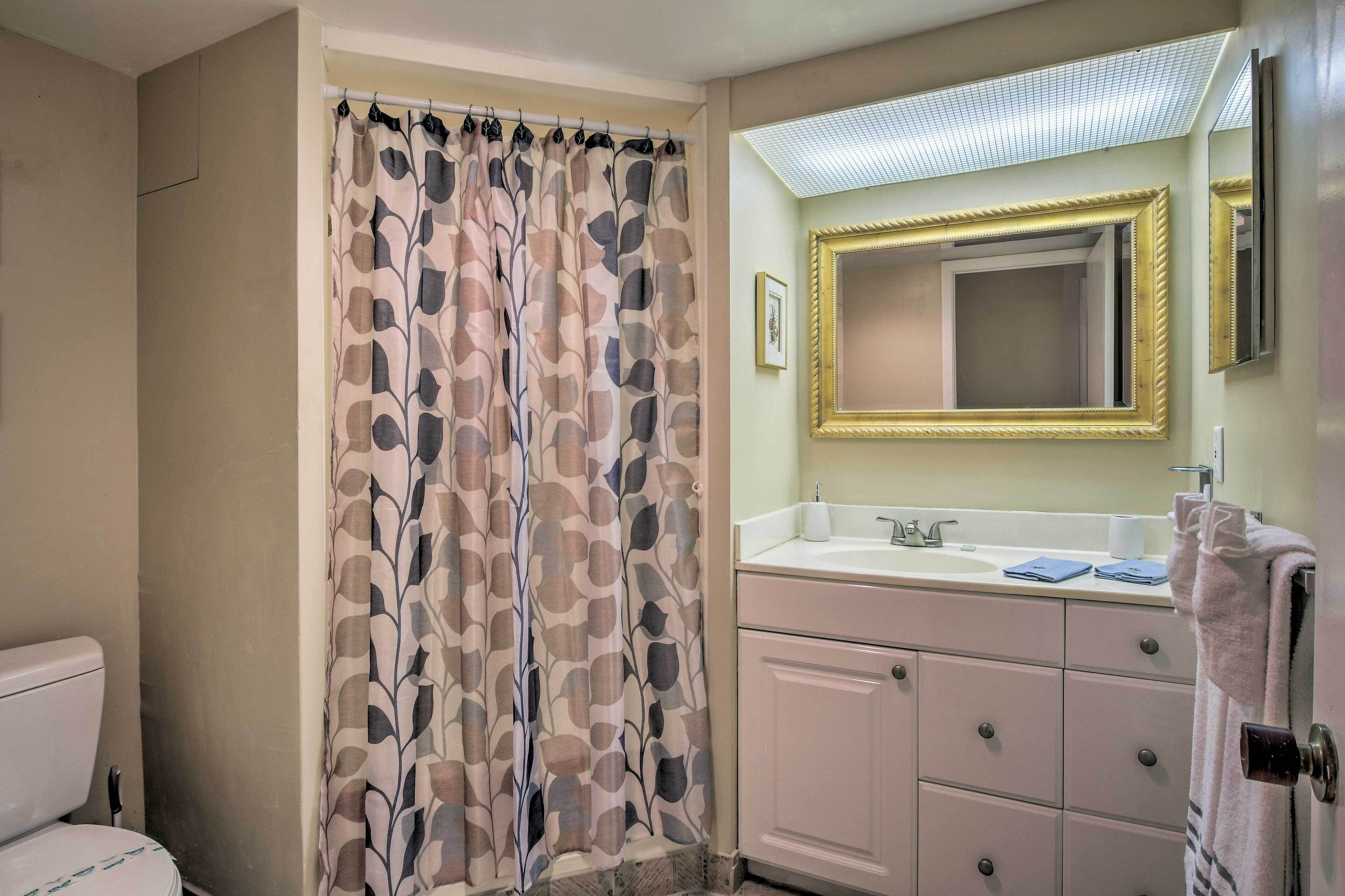 A bathroom with a shower curtain, a sink with a mirror, and a toilet.