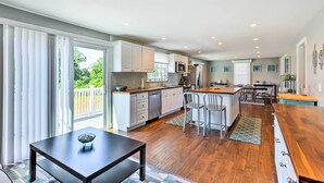A modern kitchen with white cabinets, a central island, and a dining area with chairs. - Fantastic Plymouth House w/ Deck & Ocean Views! (Plymouth)