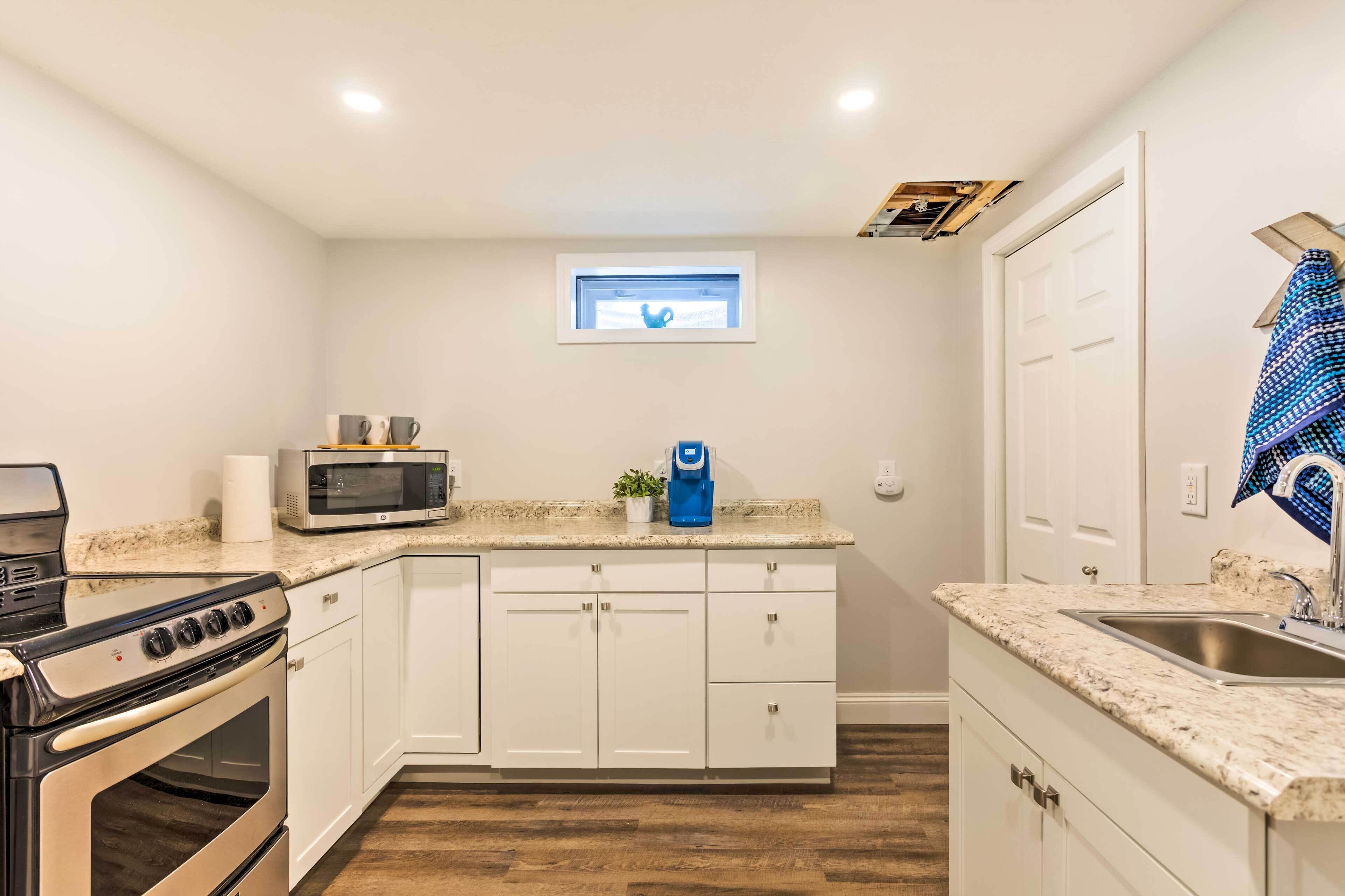 A compact kitchen with white cabinets, a built-in microwave, a stove, and a small window above the sink.