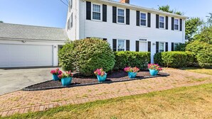 A two-story white house with a garage, surrounded by well-maintained hedges and flower pots. - Fantastic Plymouth House w/ Deck & Ocean Views! (Plymouth)