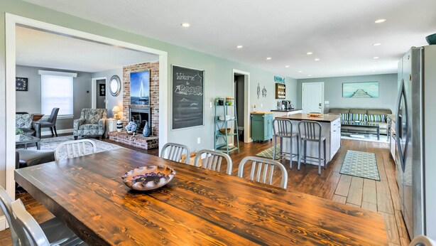 A spacious living area with a wooden dining table, a fireplace, and a kitchen area with a refrigerator. - Fantastic Plymouth House w/ Deck & Ocean Views! (Plymouth)