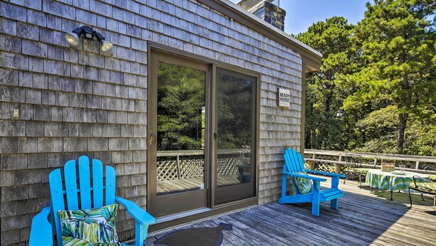 A wooden deck with two blue Adirondack chairs and a table with a green and white striped tablecloth. - Great for Couples! Cape Cod Cottage 2 Mi to Beach (Wellfleet)