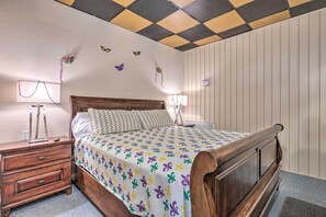 A bedroom with a wooden bed, a nightstand, a lamp, and a wall with a checkered ceiling. - 'the Float Yard' Pensacola Home w/ Pool Table (Pensacola)