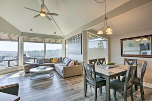 Ein geräumiger Wohnbereich mit großem Sofa, Esstisch und Stühlen. Es gibt einen Deckenventilator, große Fenster und ein Gemälde an der Wand.