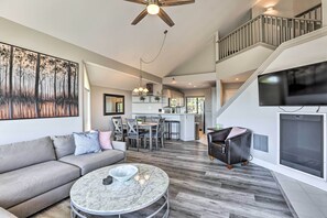A spacious living area with a gray sofa, a round marble coffee table, and a dining area with chairs. A staircase leads to an upper level with a balcony.