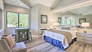 A bedroom with a large bed, a desk, and a chair, a large window, and a mirror.
