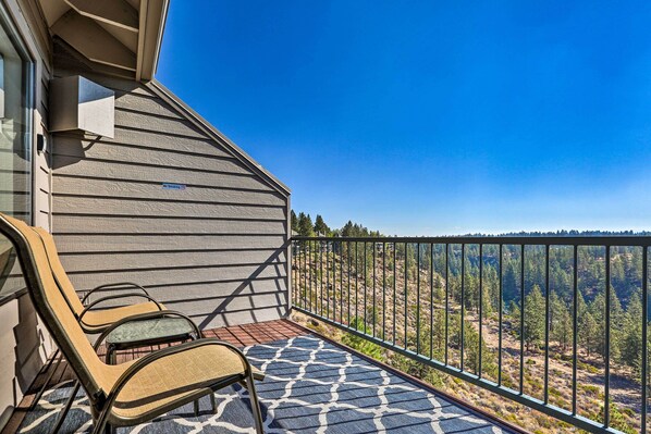 Ein Balkon mit zwei Stühlen, einem gemusterten Teppich und Blick auf eine bewaldete Landschaft.