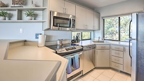 A modern kitchen with a built-in microwave, oven, and dishwasher. There are potted plants on the shelves, and a window providing natural light.