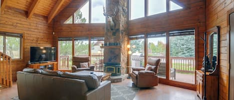 A spacious living room with a large wooden ceiling, a stone fireplace, and a television on a wooden stand.