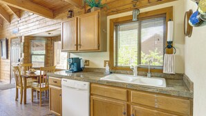 A kitchen with wooden cabinets, a granite countertop, a dishwasher, and a window with blinds.