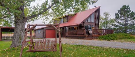 A rustic log cabin with a porch and a swing set.