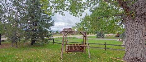 A wooden swing set in a grassy area with trees and a fence.
