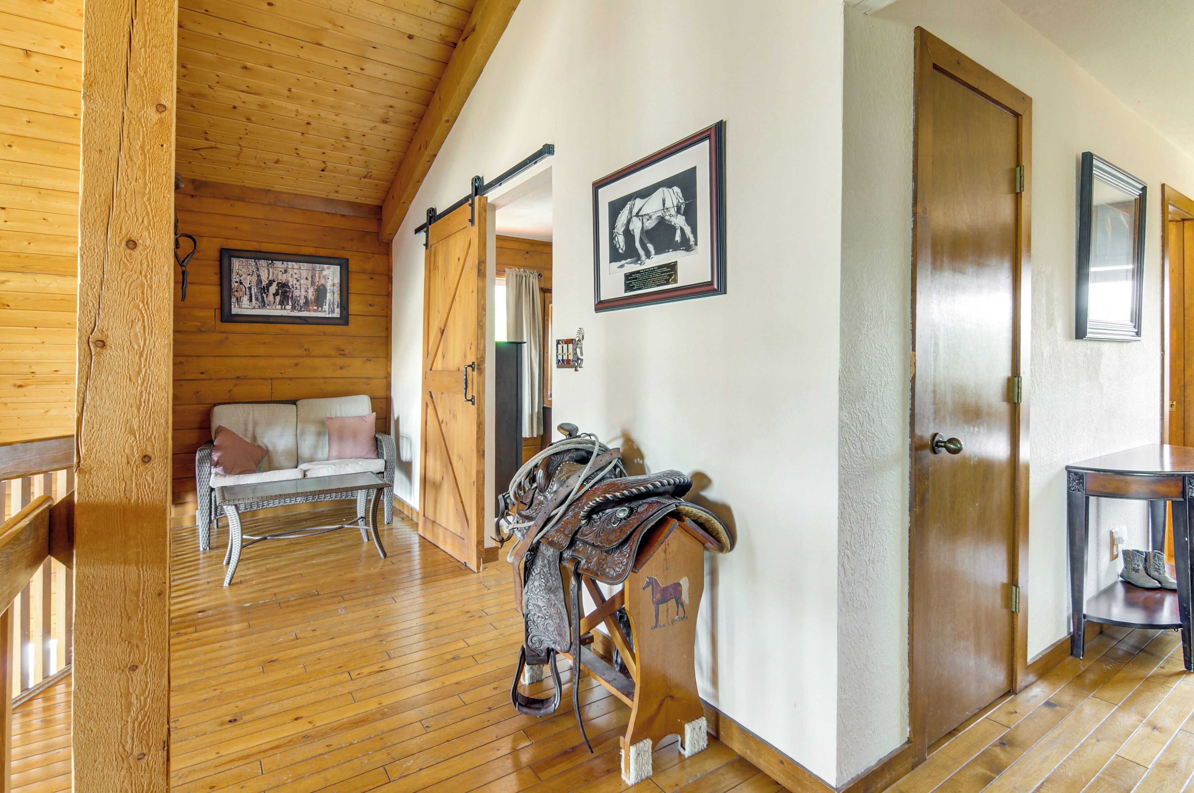 A wooden interior with a sofa, a door, a wall-mounted picture, and a saddle on a stand.