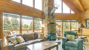 A cozy cabin interior with a stone fireplace, leather furniture, and large windows offering a view of snow-covered trees.