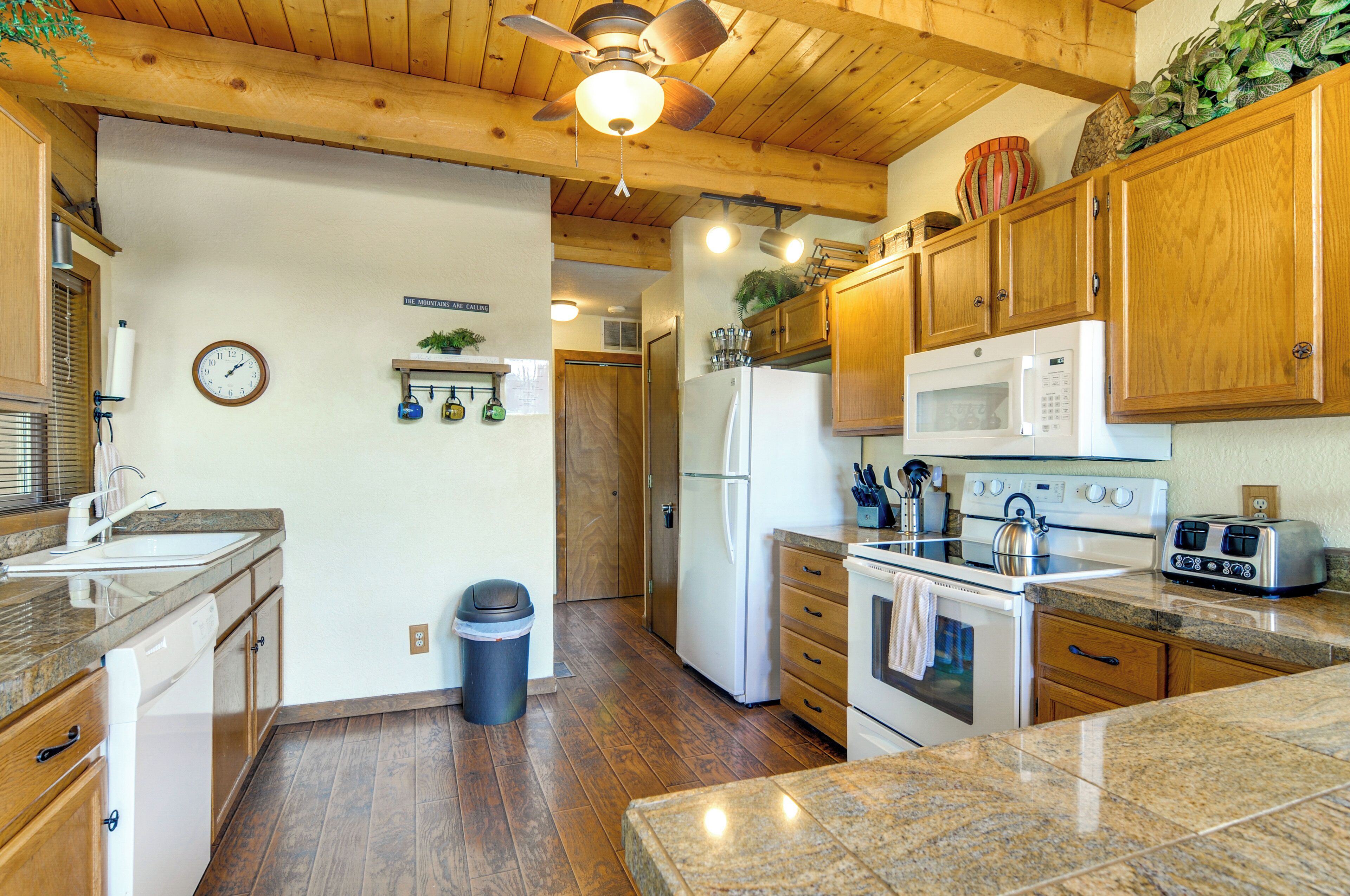 A kitchen with wooden cabinets, a microwave, a refrigerator, a stove, and a ceiling fan.