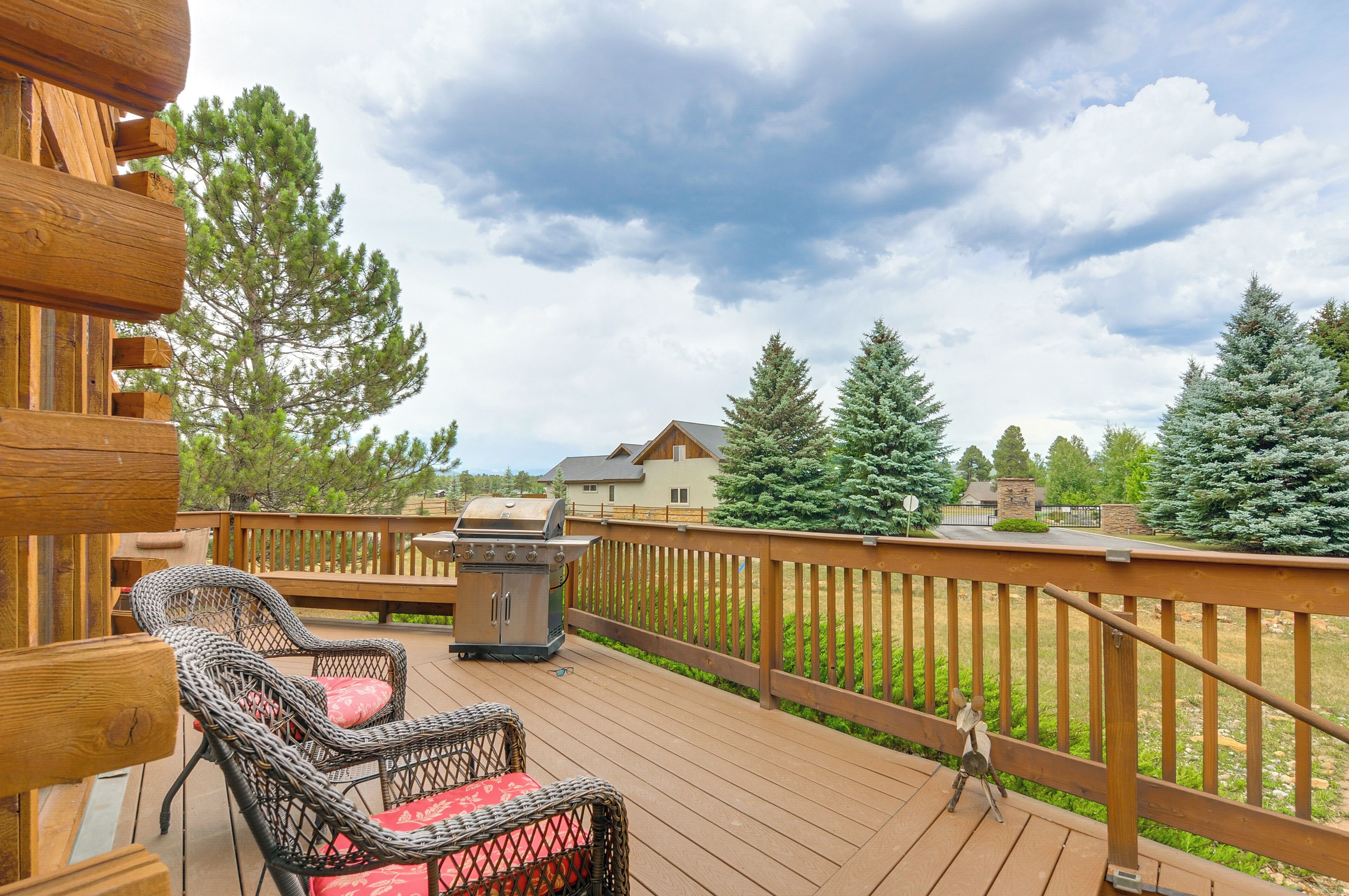 A wooden deck with wicker chairs and a grill, overlooking a residential area with houses and trees.